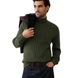 A man wears a ribbed olive green turtleneck sweater paired with dark jeans and holds a jacket over his shoulder.