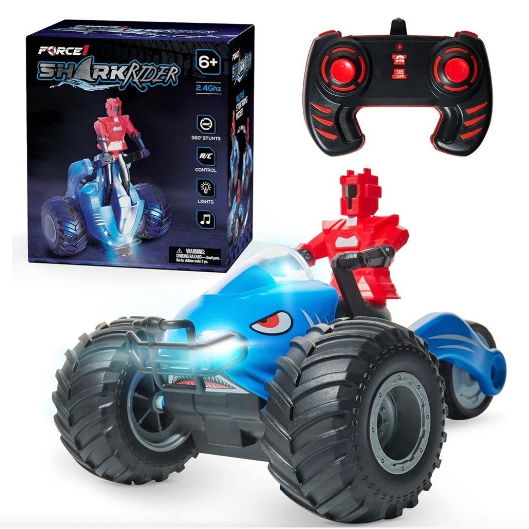 A blue and red remote-controlled toy car with shark elements and oversized rubber wheels, accompanied by a black and red two-joystick remote control.