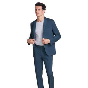 A man is wearing a teal suit with a jacket and pants, paired with a light gray t-shirt.