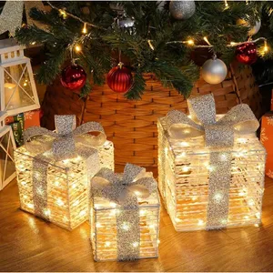 Three illuminated decorative gift boxes with silver ribbons are placed under a Christmas tree, surrounded by ornaments and holiday lanterns.