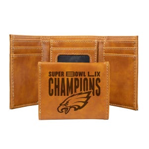 A brown leather trifold wallet with the text \“SUPER BOWL LIX CHAMPIONS\“ and an eagle logo engraved on the front. It has multiple card slots and an ID window.