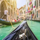 A gondola navigates a Venetian canal lined with historic buildings, vibrant flowers, and bridge.
