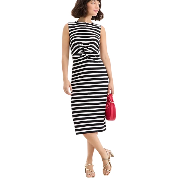 A woman is wearing a black and white striped, sleeveless midi dress with a knot detail at the waist, paired with gold strappy sandals and holding a red handbag.