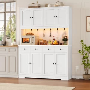 White kitchen cabinet with upper and lower storage, featuring black handles. Middle section displays a microwave and various kitchen items, including utensils and food products. Decor includes a plant, flowers, and bottles.