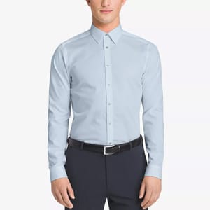 A man is wearing a light blue dress shirt and dark trousers with a black belt.