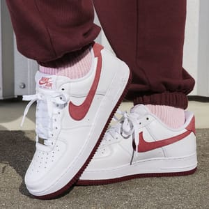 White and red Nike Air Force 1 sneakers worn with pink socks and burgundy pants.