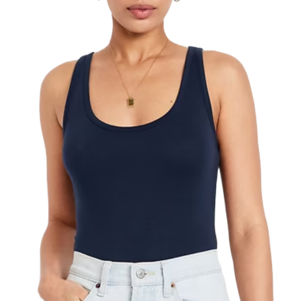 A woman is wearing a navy blue tank top and light blue jeans, complemented by a gold necklace with a rectangular pendant.