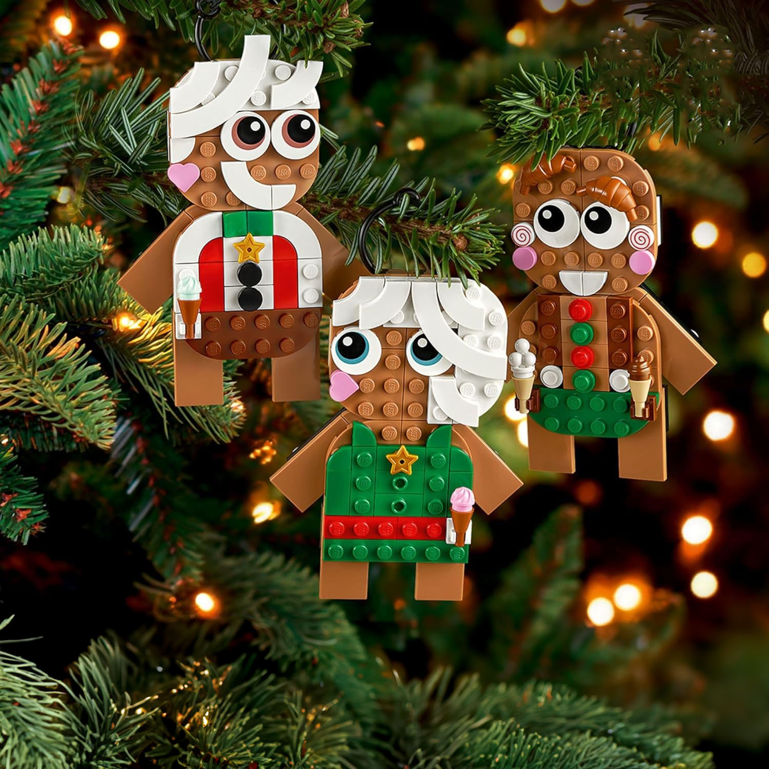 Three LEGO holiday ornaments designed to resemble gingerbread people are hanging on a Christmas tree.