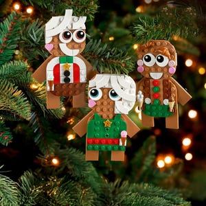 Three LEGO holiday ornaments designed to resemble gingerbread people are hanging on a Christmas tree.