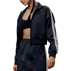 A person is wearing a black athletic jacket and matching pants with white side stripes, paired with a black sports bra.