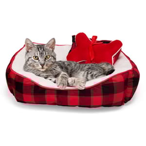 A gray tabby cat is lounging in a red and black plaid pet bed with a plush interior, accompanied by a red bow-shaped pillow.