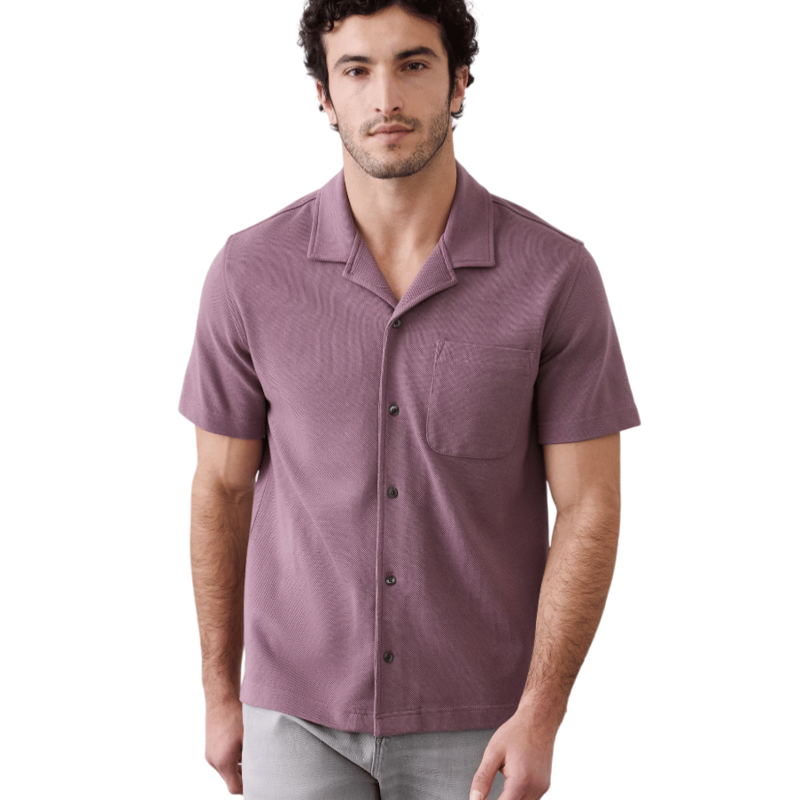 A man is wearing a short-sleeve, button-up shirt in a textured mauve color with a single chest pocket. He pairs it with light gray pants.