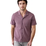 A man is wearing a short-sleeve, button-up shirt in a textured mauve color with a single chest pocket. He pairs it with light gray pants.