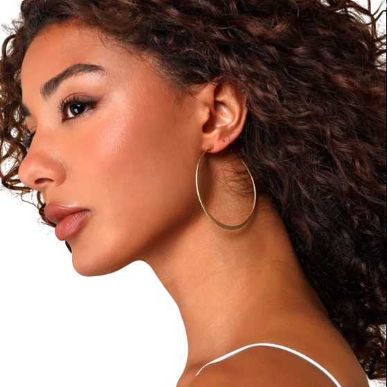 A woman with curly hair wears large gold hoop earrings and a white spaghetti strap top.