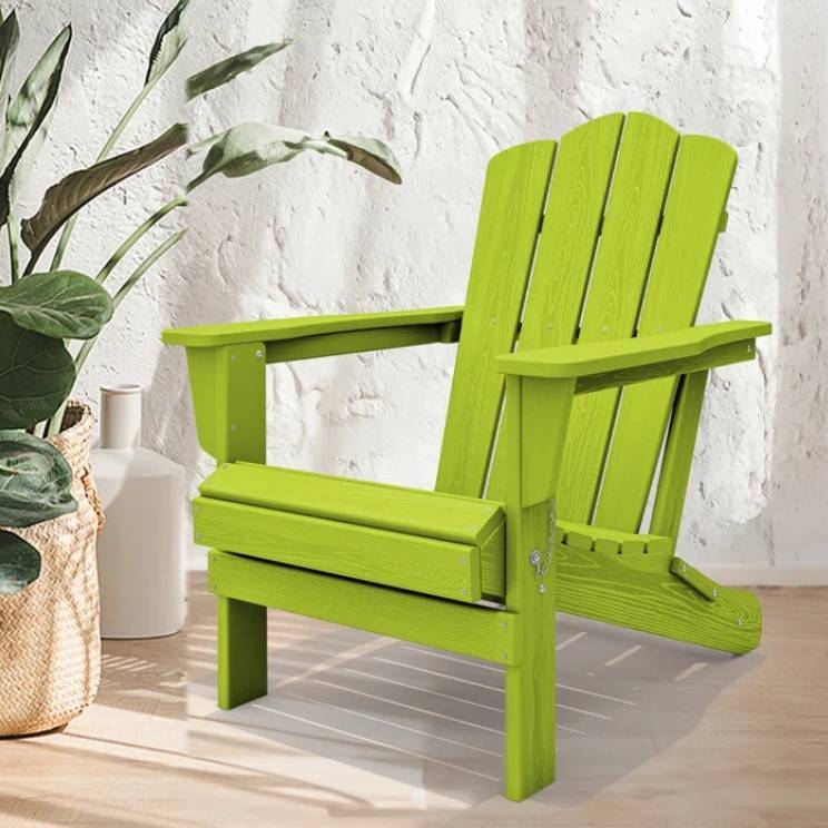Bright green Adirondack chair with a classic slatted design, featuring a high back and wide armrests, placed on a light wooden floor against a textured white wall and next to a potted plant.