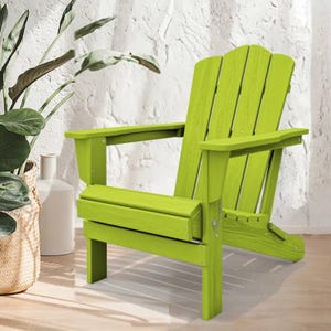 Bright green Adirondack chair with a classic slatted design, featuring a high back and wide armrests, placed on a light wooden floor against a textured white wall and next to a potted plant.