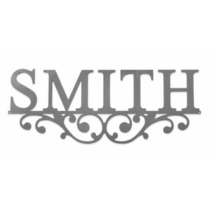 A decorative metal wall sign featuring the name \“SMITH\“ with ornate swirl accents below.