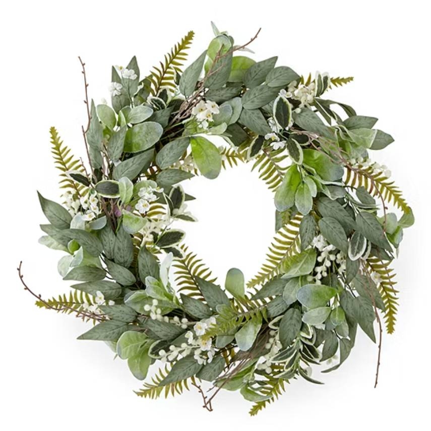 A lush wreath featuring a mix of green foliage, including fern leaves and eucalyptus, interspersed with small white blossoms on a circular frame.