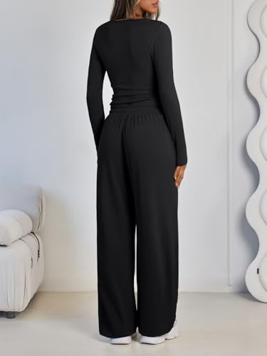 A person is wearing a black long-sleeve top and wide-leg pants, standing with their back to the camera. The outfit is paired with white shoes in a modern, minimalist room setting.