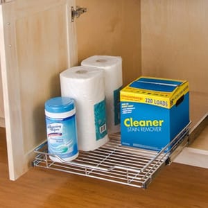 A roll-out wire shelf in a cabinet holding laundry detergent, paper towels, and stain remover.