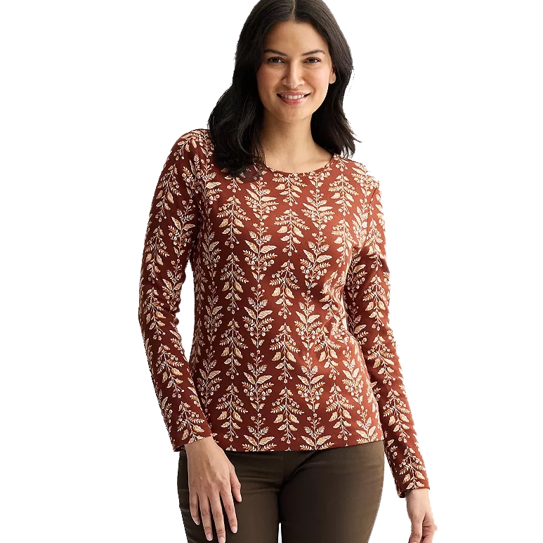 A woman is wearing a long-sleeve top with a brown base and a white leaf pattern, paired with dark pants.