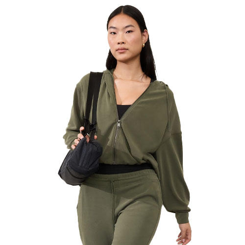 A woman is wearing an olive green Seasoft Bubble Hem Jacket with a relaxed fit and a front zipper. She carries a black crossbody bag, and the outfit includes matching olive green pants.