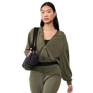 A woman is wearing an olive green Seasoft Bubble Hem Jacket with a relaxed fit and a front zipper. She carries a black crossbody bag, and the outfit includes matching olive green pants.