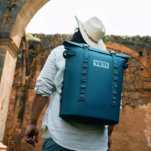 A person carrying a blue YETI backpack cooler on their back.