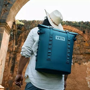 A person carrying a blue YETI backpack cooler on their back.