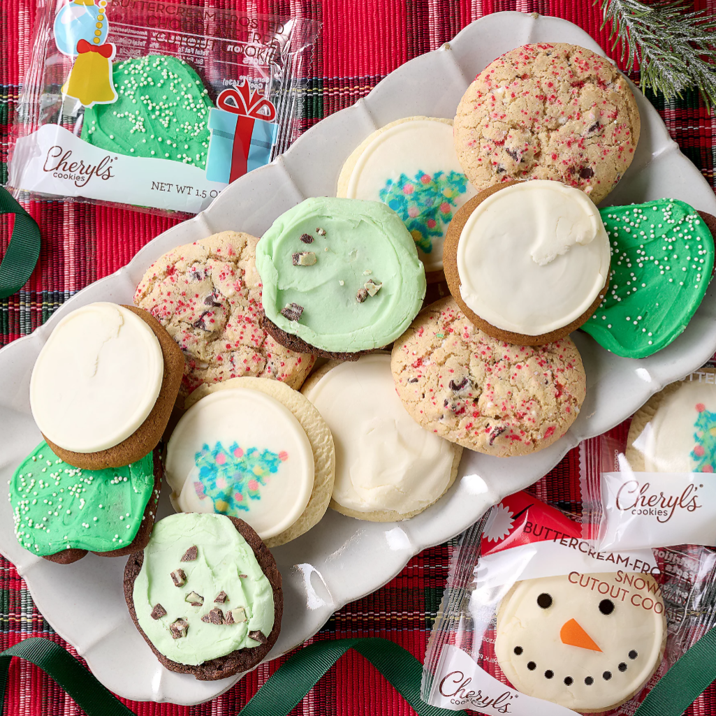 A platter of Cheryl’s holiday-themed cookies includes frosted cookies with various designs like snowflakes and a snowman, presented on a festive red and green plaid background.