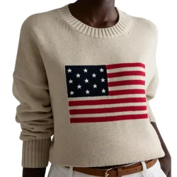 A beige sweater with a large U.S. flag design on the front, featuring red stripes and white stars on a navy blue field. The sweater is paired with a brown belt and white pants.