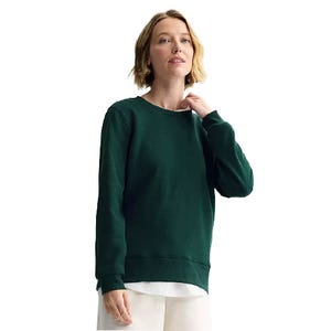 A person is wearing a green long-sleeve pullover sweater over a white shirt. The outfit is paired with light-colored pants.