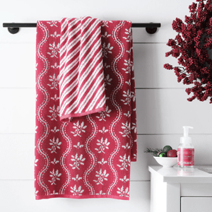 A set of two Martha Stewart bath towels, one with a red and white floral pattern and the other with diagonal stripes, displayed on a black towel bar next to a seasonal decoration and soap dispenser.