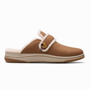Clarks Cozy Cloudstepper Slippers are tan slip-ons with a fluffy lining, featuring a button detail and a cushioned sole for comfort and support.