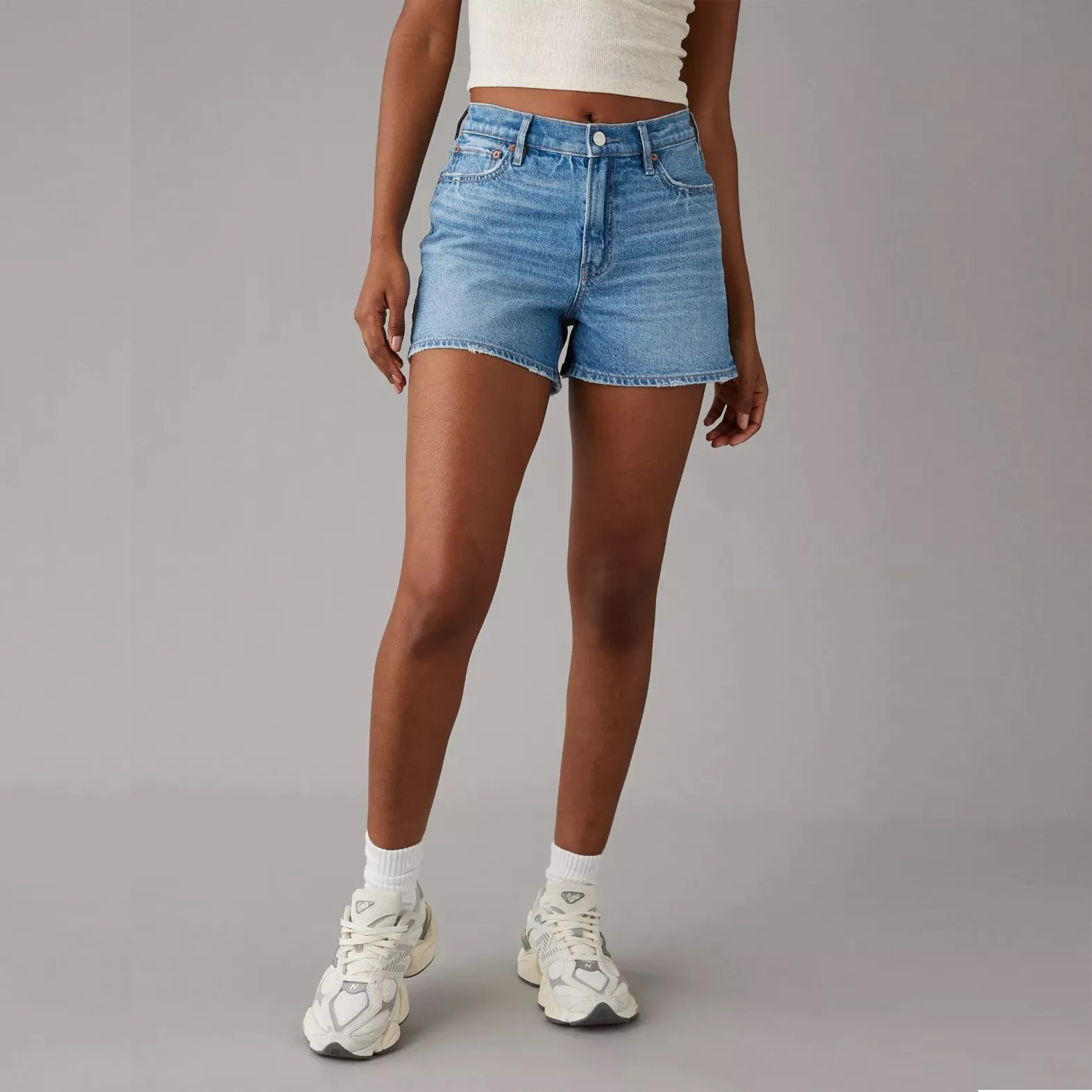 A person is wearing blue denim shorts and white chunky sneakers.