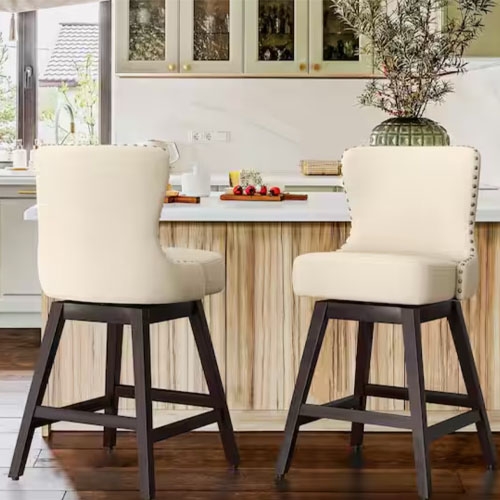 This image shows two swivel bar stools with cream-colored upholstered seats and backs, featuring nailhead trim. They have dark wooden legs with a footrest and a slightly tapered design.