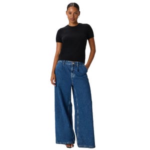 A person is wearing a black short-sleeve T-shirt and blue wide-leg jeans with hands in pockets.