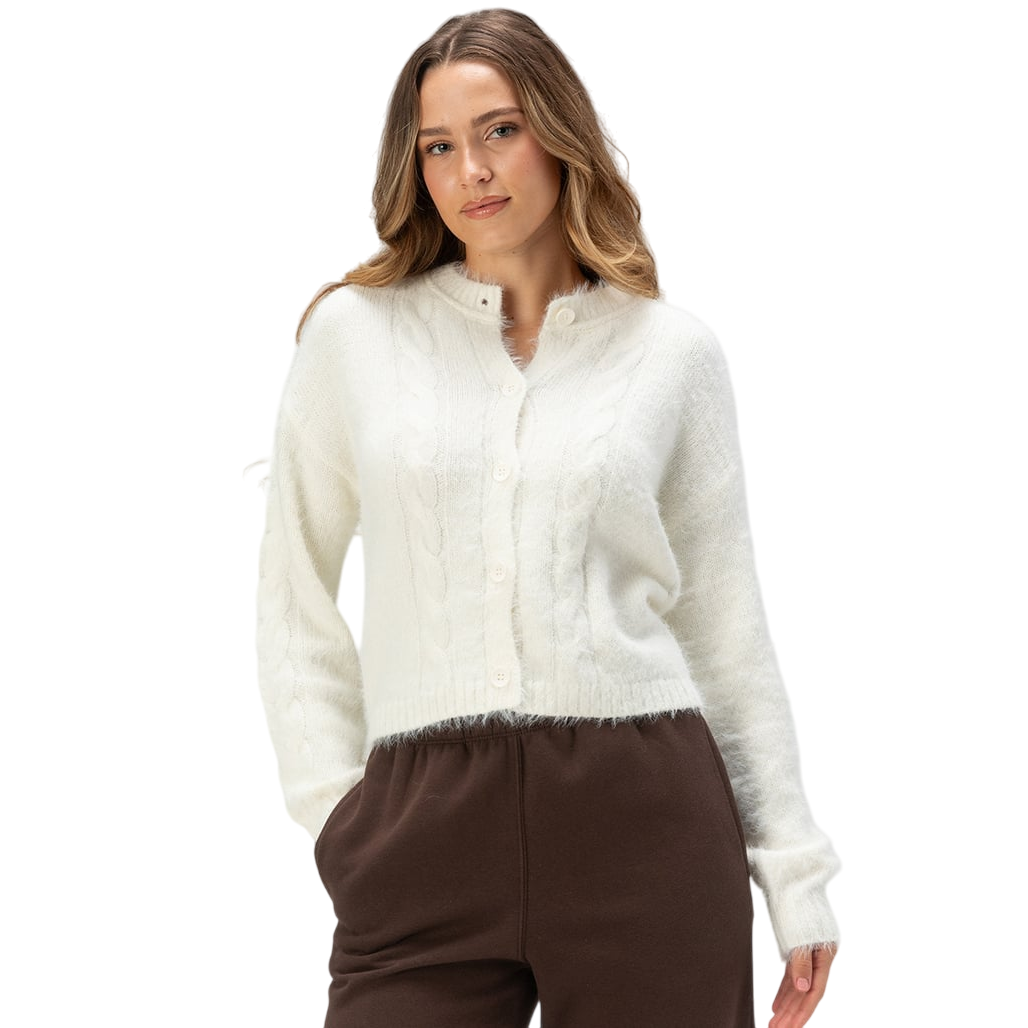 A woman wearing a white cable-knit cardigan and brown pants.