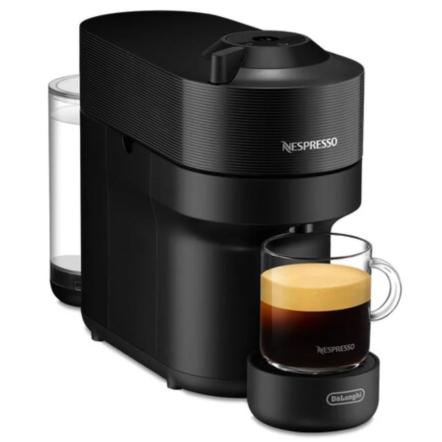 A sleek black Nespresso espresso machine with a compact design, featuring a removable water tank on the side and a clear glass cup with espresso on a branded coaster.