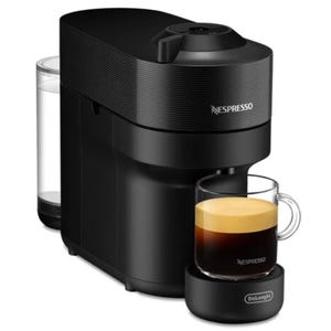 A sleek black Nespresso espresso machine with a compact design, featuring a removable water tank on the side and a clear glass cup with espresso on a branded coaster.