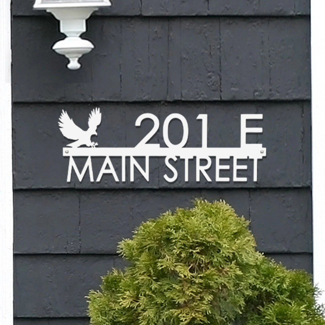 House number sign with \“201 E Main Street\“ featuring an eagle silhouette, mounted on dark siding.