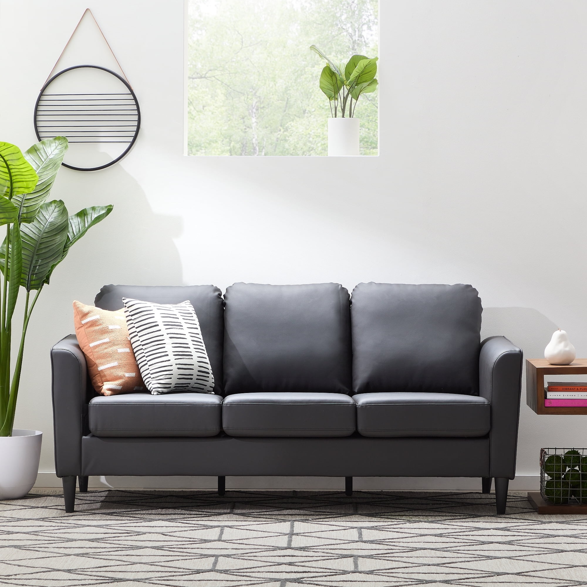 A black leather sofa with decorative pillows, a white vase with greenery, and a small end table with books and a decorative object.