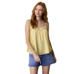 A woman in a sleeveless yellow top with lace trim and denim shorts, posing against a neutral background.