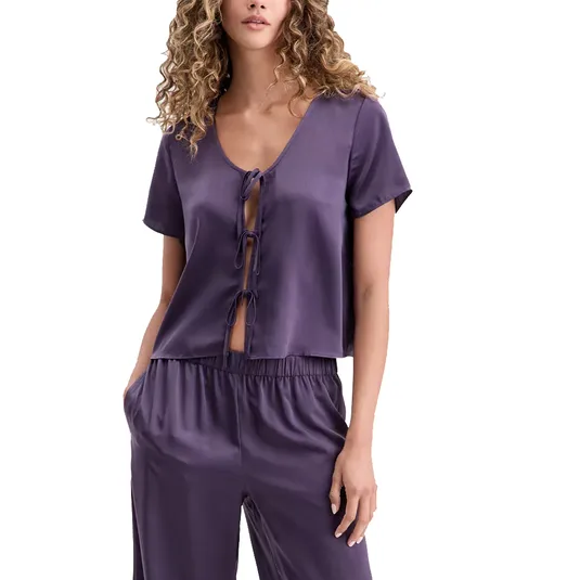 A woman is wearing a short-sleeved, purple satin pajama set with front tie closures and matching pants.