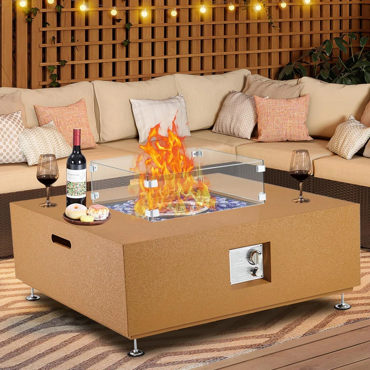 Outdoor fire pit table with glass wind guard, placed in a cozy seating area with a bottle of wine, glasses, and snacks on top.