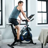 A person is cycling on a Horizon Fitness 5.0 IC indoor exercise bike, positioned in a bright, modern room with large windows and a minimalist decor.