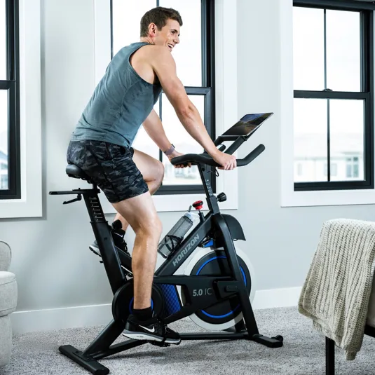 A person is cycling on a Horizon Fitness 5.0 IC indoor exercise bike, positioned in a bright, modern room with large windows and a minimalist decor.