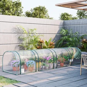 A transparent greenhouse tunnel with various potted plants and flowers is shown on a modern patio, surrounded by lush greenery and a concrete wall.