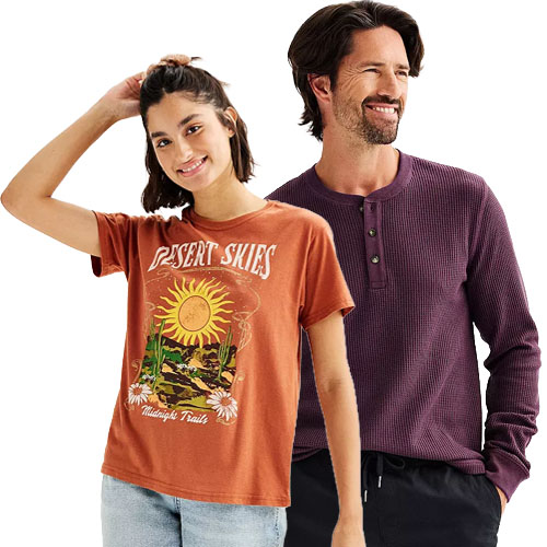 A woman wearing a rust-colored \“Desert Skies\“ graphic t-shirt and a man in a burgundy henley long-sleeve shirt and black pants, both smiling.