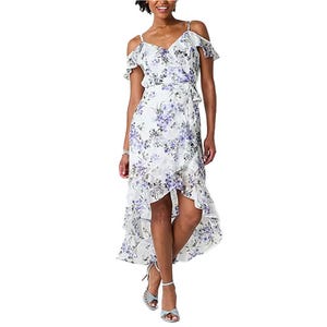 A woman is wearing a floral cold-shoulder dress with ruffled details and an asymmetrical hem, paired with strappy high-heel sandals.